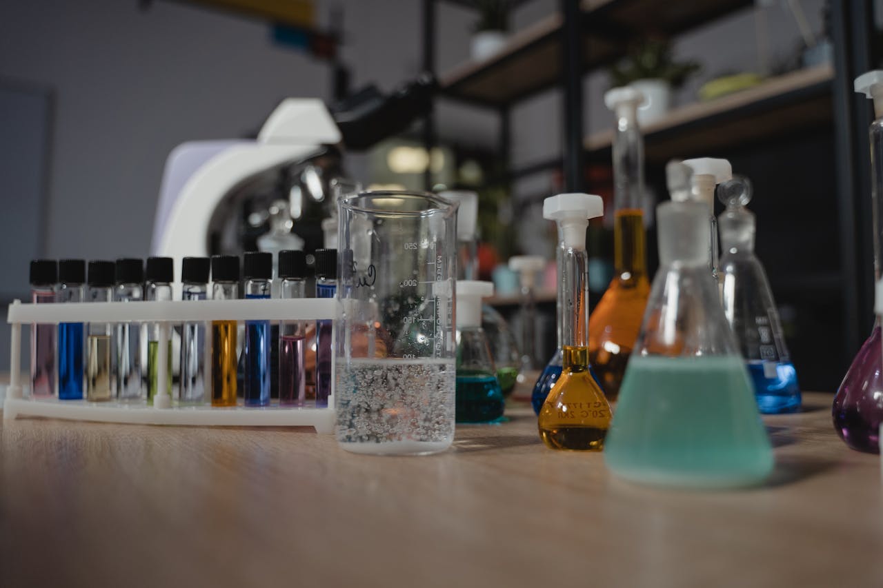 Glassware with colored liquids in a laboratory on a wooden table, showcasing diverse chemical research tools.